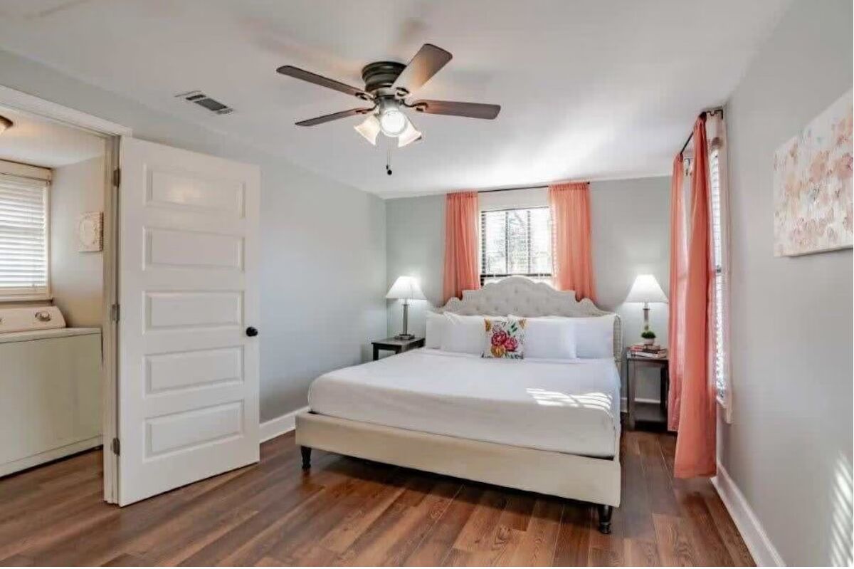 Un dormitorio con cama, ventilador de techo, ventana con cortinas y puerta.
