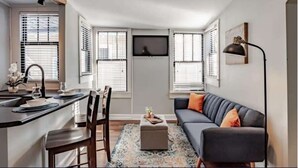 A modern kitchen with a dining area, a gray sofa, and a small table with a plant. - Dauphin Darling 4 Units  (Mobile)