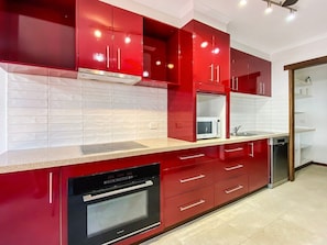 A modern kitchen with red cabinetry, a microwave, a dishwasher, and a built-in oven.