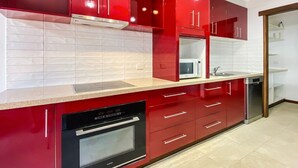 Une cuisine moderne avec des meubles de rangement rouges, un four à micro-ondes, un lave-vaisselle et un four encastré.