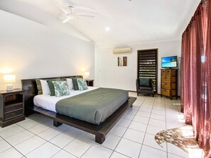 A bedroom with a bed, nightstands, a TV, and a window with blinds.