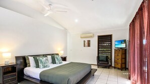 Une chambre à coucher avec un lit, des tables de chevet, une télévision et une fenêtre avec des stores.