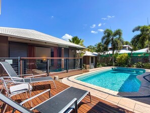 Una piscina con sillas de descanso, una terraza de madera y una casa con techo de metal.