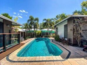 A rectangular swimming pool with a tiled deck, surrounded by a wooden fence and various plants.