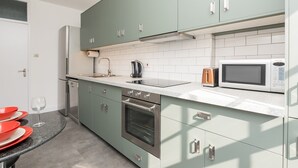 Ett modernt kök med turkosa skåp, en ugn i rostfritt stål, en mikrovågsugn och en kaffebryggare.