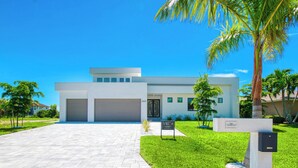 A modern two-story building with a flat roof, large garage doors, and a well-maintained lawn with palm trees. - VRCC Villa Sogno - modern-day getaway (Cape Coral)