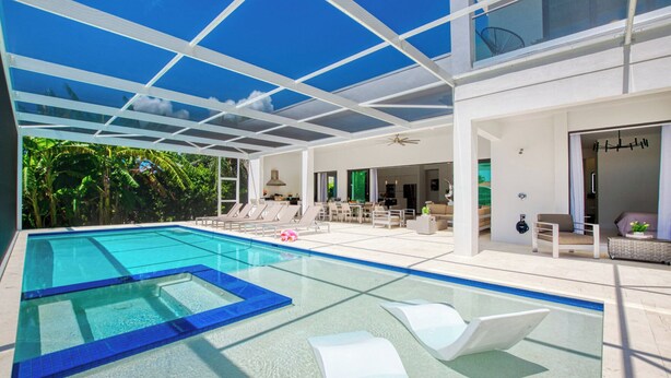 A modern indoor swimming pool with clear blue water, surrounded by white lounge chairs and a glass ceiling. - VRCC Villa Sogno - modern-day getaway (Cape Coral)