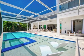 Une piscine intérieure moderne, avec une eau d’un bleu cristallin, entourée de chaises longues blanches et dotée d’un plafond en verre.