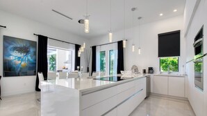 A modern kitchen with a central island, pendant lighting, and a large window. - VRCC Villa Sogno - modern-day getaway (Cape Coral)