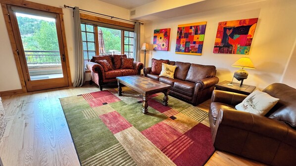 A living room with a large window, two sofas, a coffee table, and colorful artwork on the wall.