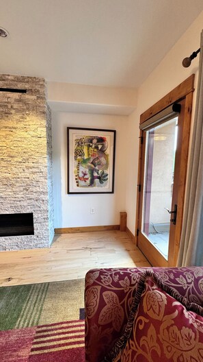 Ein Wohnzimmer mit einer Steinwand, einem gerahmten abstrakten Gemälde, einer Holztür und einem gemusterten Sofa.