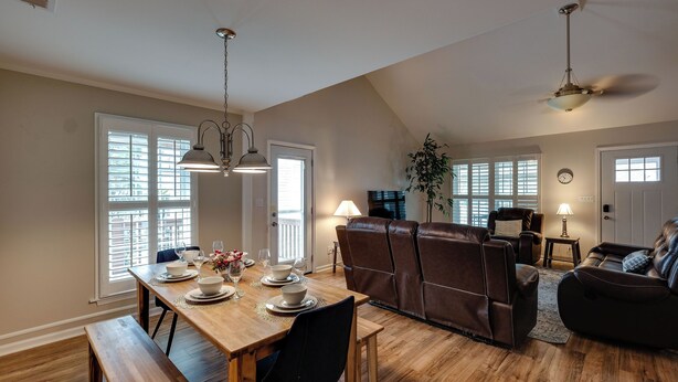 A dining area with a wooden table set for four, a brown leather sofa, and a ceiling fan. - Refresh at Rivermist 2 Units with Pool (Savannah)