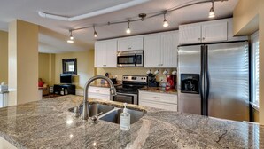 A modern kitchen with granite countertops, stainless steel appliances, and a large island with a sink. - Refresh at Rivermist 2 Units with Pool (Savannah)