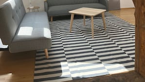 Ein modernes Schlafzimmer im Loft-Stil mit schrägem Dach, einem grauen Sofa, einem kleinen Holztisch und einem Streifenmuster-Teppich.