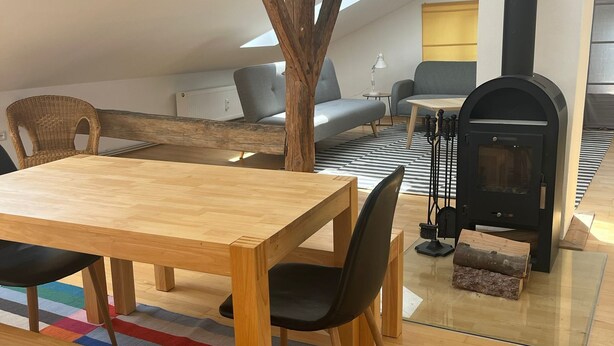 Ein gemütliches Schlafzimmer im Loft-Stil mit einem Holzesstisch, einem farbenfrohen StreifenTeppich und einem schwarzen Kaminofen.