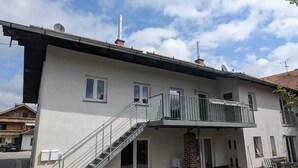 A two-story building with a balcony, a staircase, and a paved courtyard. - Lake Starnberg: Terraces, wood-burning stove  (Münsing)