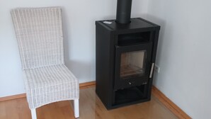 A white wicker chair next to a black wood-burning stove in a room with wooden flooring. - Lake Starnberg: Terraces, wood-burning stove  (Münsing)