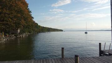 Eine Holzsteg, der sich in einen ruhigen See erstreckt, mit einem Segelboot in der Ferne.
