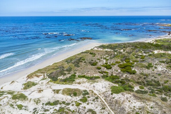 A coastal landscape with a beach, rocky outcrops, and sparse vegetation.