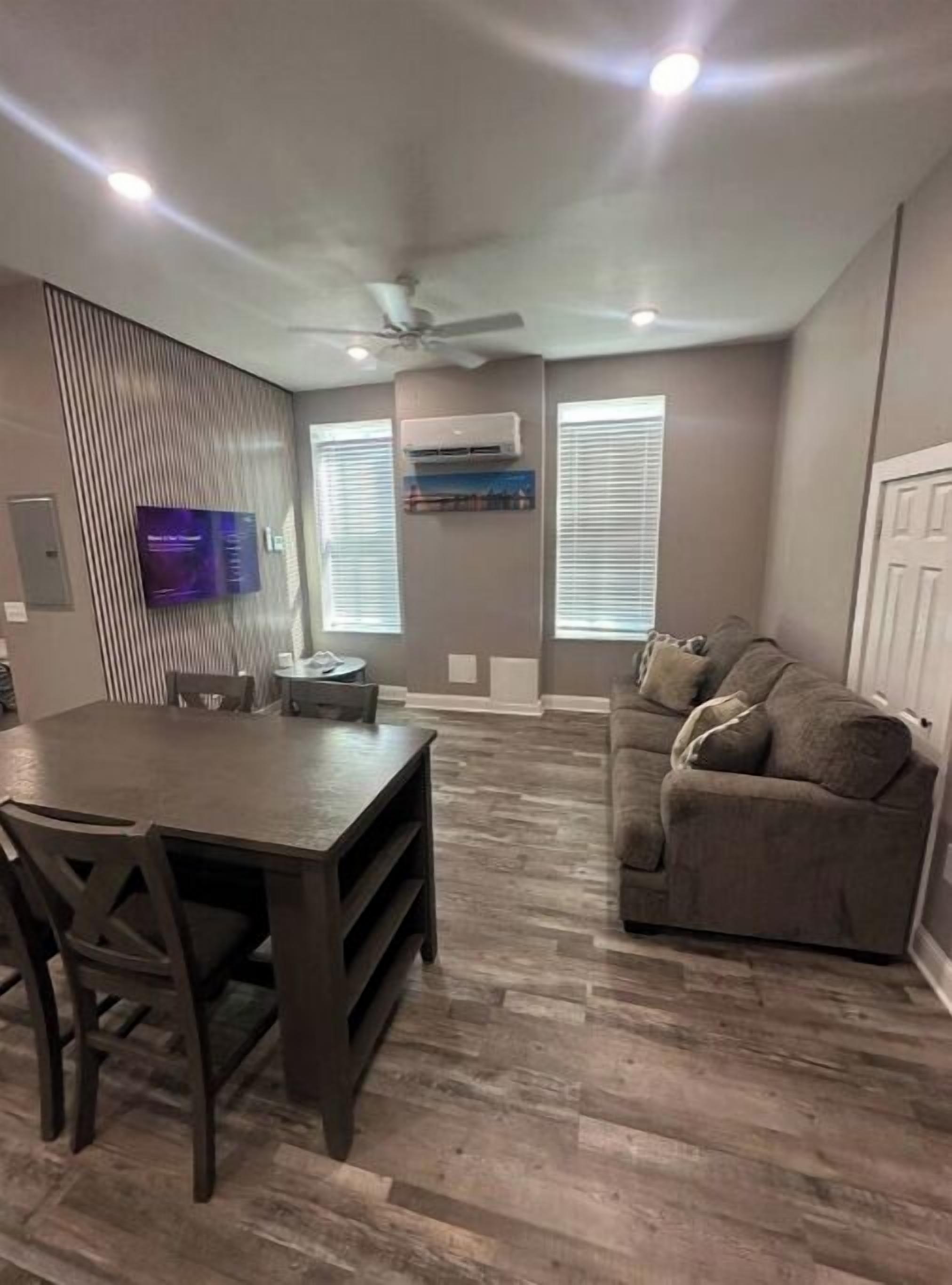 Una sala de estar moderna con comedor, un sofá gris y un televisor de pantalla plana montado en la pared.