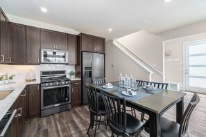 A modern kitchen with dark wood cabinets, stainless steel appliances, and a dining area with a wooden table and black chairs. - Welcoming Modern Cabin: Free Resort Shuttle right outside! (Fraser)