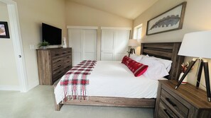 Un dormitorio con cama, cómoda, televisor y lámpara.