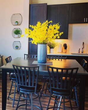 A modern kitchen with dark cabinets, a central island with a vase of yellow flowers, and a dining area with black chairs. - Welcoming Modern Cabin: Free Resort Shuttle right outside! (Fraser)