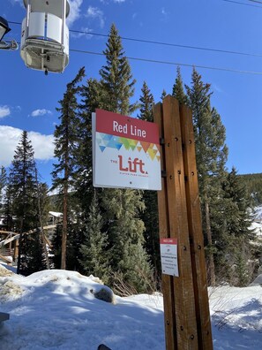 Señal de Red Line Lift sobre un poste de madera, rodeada de nieve y árboles.