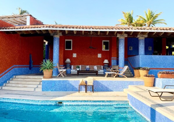 A pool area with a red and blue building, a sofa, and lounge chairs. - Villa 4 Rec. con Vistas y Playa Privada (Santa María Huatulco)