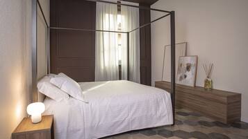 A bedroom with a four-poster bed, a bedside table with a lamp, a wooden bench, and a framed picture on the wall.