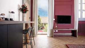 Una sala de estar moderna con televisor, un comedor con sillas, un florero con flores y vistas al exterior.