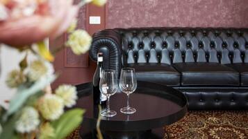 A room with a black leather sofa, a round black table with two wine glasses, and a floral arrangement.
