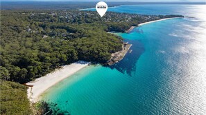 An aerial view of Jervis Bay with a beach, clear turquoise waters, and dense forested areas.