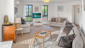 A living room with a sofa, a coffee table, a TV, and a wooden cabinet. - Milo's @ the Bay by Experience Jervis Bay (Vincentia)