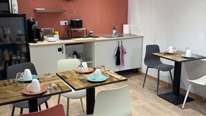 Une cuisine moderne équipée d’une horloge, d’un four à micro-ondes et d’une machine à café. On y trouve des tables à manger avec des chaises et un évier.
