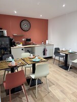 Una cocina moderna con un reloj, microondas y cafetera. Hay mesas de comedor con sillas y un lavamanos.