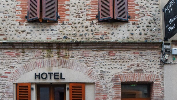 La façade d’un hôtel, avec un revêtement en briques, des volets en bois et une enseigne indiquant le nom de l’hôtel.