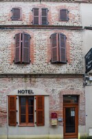 Fachada de hotel con revestimiento de ladrillo, contraventanas de madera y un cartel con el nombre del hotel.