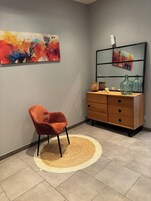 Una habitación con un aparador de madera, una silla, un tapete redondo y dos cuadros abstractos en la pared.