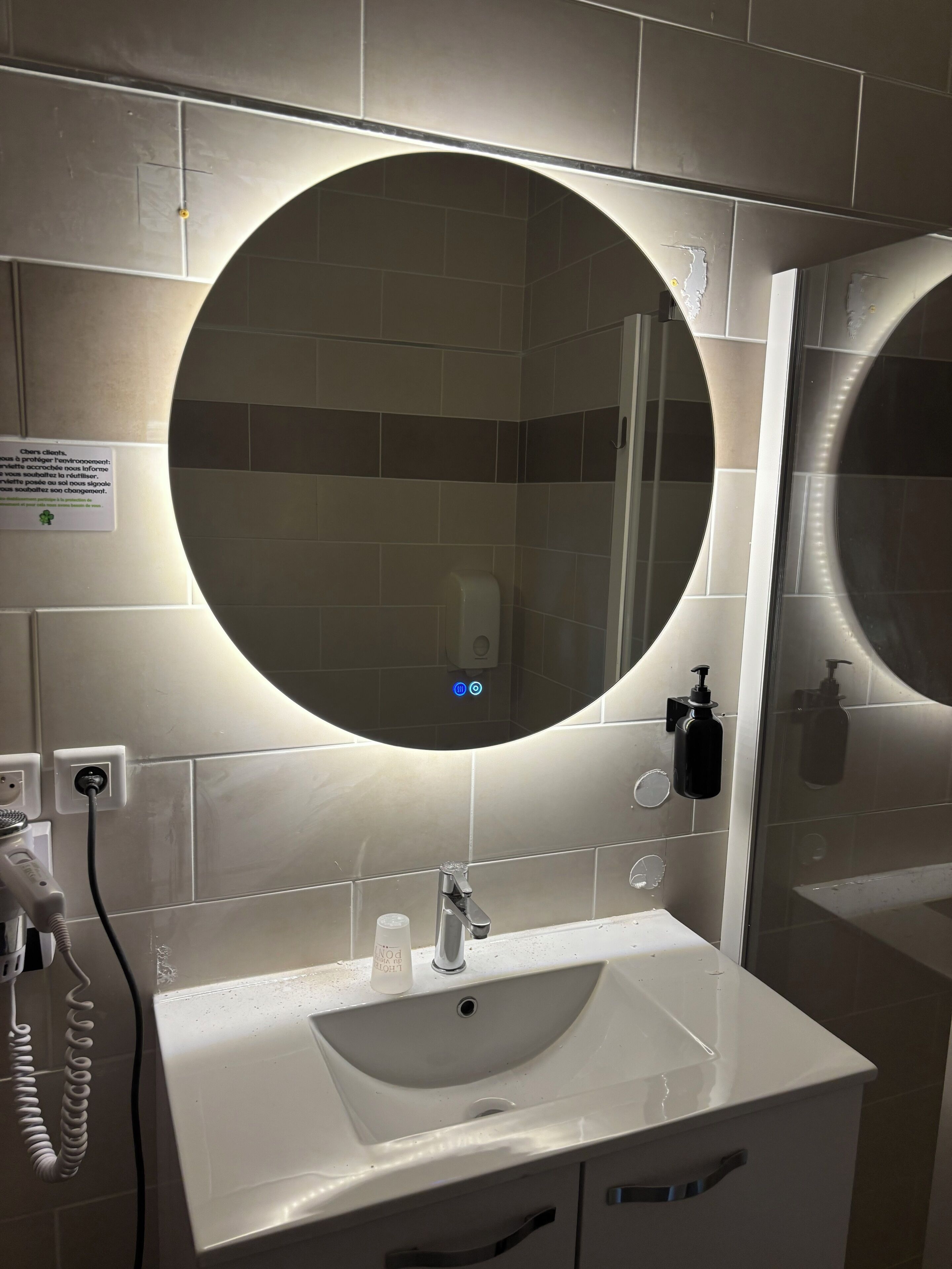 A bathroom with a white sink, a round mirror, and a hand dryer.