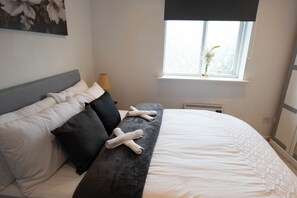 A neatly made bed with white bedding, a grey headboard, and a bench with rolled towels. - Beckton Docklands - 1 Bedroom - Sleeps 4 - Wifi (London)
