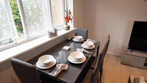 A dining area with a table set for four, positioned near a window with a view of greenery. - Beckton Docklands - 1 Bedroom - Sleeps 4 - Wifi (London)