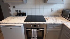 A kitchen with a white marble countertop, a black induction cooktop, a stainless steel oven, and a built-in microwave. - Beckton Docklands - 1 Bedroom - Sleeps 4 - Wifi (London)