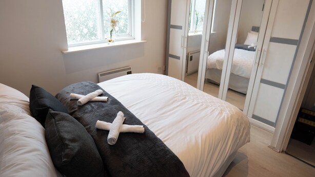 A bedroom with a bed, pillows, a window with a plant, and a wardrobe with sliding doors. - Beckton Docklands - 1 Bedroom - Sleeps 4 - Wifi (London)