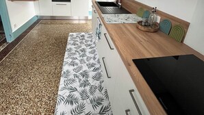 Une cuisine moderne avec des meubles blancs, un plan de travail en bois, un four encastré et une plaque de cuisson noire.