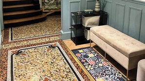 Un escalier recouvert d’une moquette à motifs menant à un palier où se trouvent un banc et une petite table.