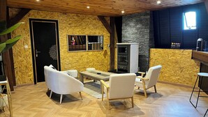 Une pièce chaleureuse avec un plafond en bois, un mur en pierre et une porte noire. On y trouve un canapé blanc, une petite table et un comptoir de bar.