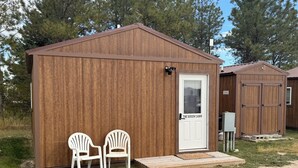 A small wooden cabin with a white door labeled "The Queen Cabin." There are two white plastic chairs outside. - O’Neill Ventures’s Queen Cabin with WIFI (Martin)