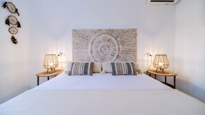 Camera da letto con un letto grande, due comodini con lampade, un condizionatore d'aria a muro e un’opera d’arte circolare appesa al muro.