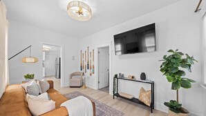 A modern living room with a brown sofa, a large flat-screen TV, a ceiling light fixture, and a potted plant. - Comfortable 2- Bedroom House In Cleveland 1330 (Cleveland)